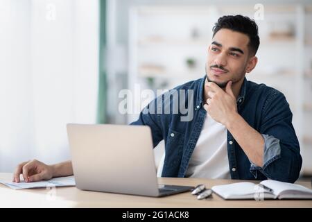 Dreamy young man sitting at office, looking at copy space Stock Photo