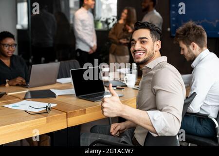 Arab businesman sitting at desk showing thumbs up gesture Stock Photo