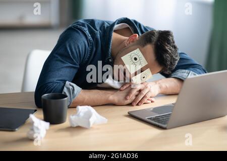 Exhausted arab guy with eyes drawing sleeping at workdesk Stock Photo