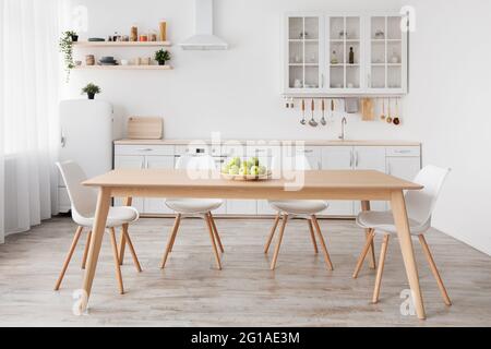 Light scandinavian kitchen interior. White furniture with various utensils, wooden table and chairs in dining room Stock Photo