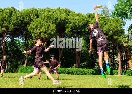 Group of young teenagers people in team wear playing a frisbee game in park oudoors. jumping man catch a frisbee to a teammate in an ultimate frisbee Stock Photo