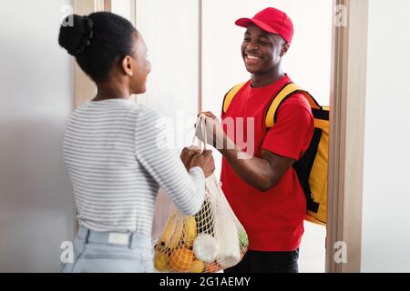 Black Woman Receiving Grocery Shopping Bag From Courier At Home Stock Photo