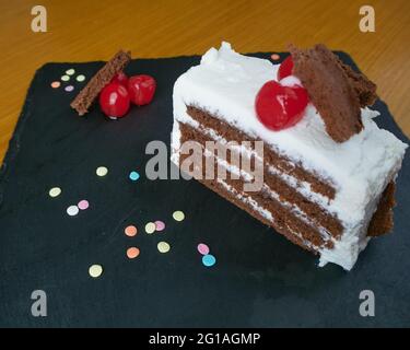 Black forest slice decorated with cherries, small pieces of cake and decorative and colorful sugar sprinkles on a black slate board Stock Photo