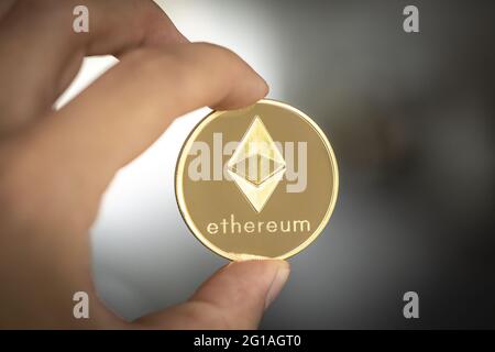 Ethereum cryptocurrency, physical coin held between two fingers. Stock Photo