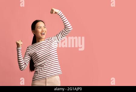 Overjoyed Young Asian Woman Celebrating Success With Raised Fists Stock Photo