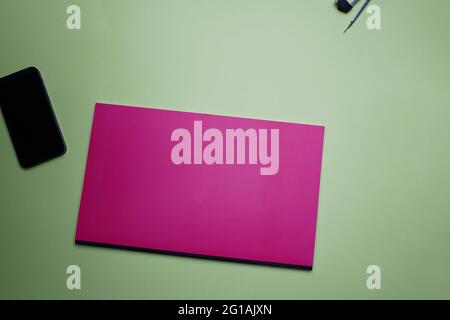 Business, office, student, education flat lay, table top. Pink notebook, compass and phone on green background Stock Photo