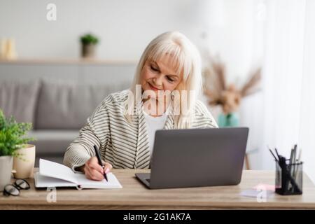 Mature woman writing and using laptop at home Stock Photo
