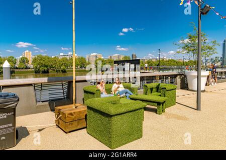 Two woman sitting on an artificial grass sofa at Circus West Village next to the River Thames at Battersea Power Station,London ,UK Stock Photo