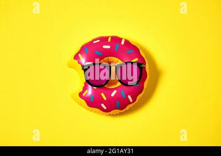 Inflatable donut in pink sunglasses on yellow background. Creative minimal concept. Top view Flat lay Stock Photo