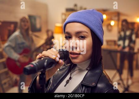 Happy young female with microphone looking at you while singing Stock Photo