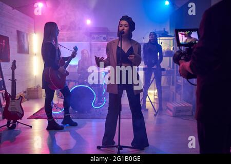 Young female singing on stage in front of cameraman shooting music video Stock Photo