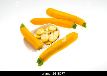 Closeup top view of ripe Yellow Zucchini,Courgette four full fruits and  slices displayed in a dish isolated against white background . Stock Photo