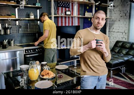 Young man with mug standing by table against another guy Stock Photo