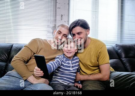 Family of three watching video in smartphone while sitting on couch Stock Photo