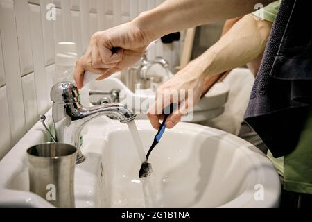 Hands of young man with toothbrush over sink in bathroom Stock Photo