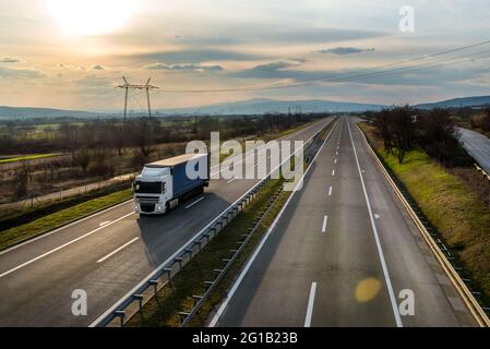 Truck with semi-trailer driving along highway on the sunset sky background. Goods delivery by roads. Services and Transport logistics Stock Photo