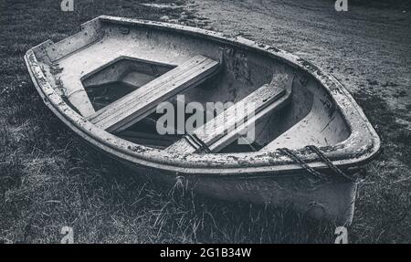 Shipwreck - Forgotten, old boat lies on a meadow by the wayside and is attacked by the weather - dark mood style. Stock Photo