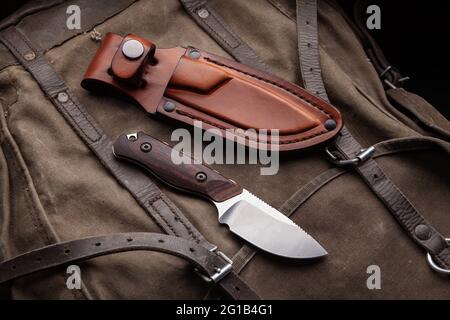 A hunting knife with a wooden handle and a leather case on a khaki canvas backpack. Weapons for self-defense and survival. Stock Photo