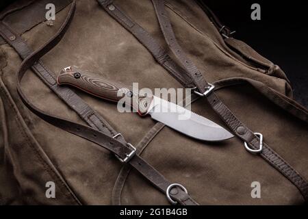 A hunting knife with a wooden handle on a khaki canvas backpack. Weapons for self-defense and survival. Stock Photo