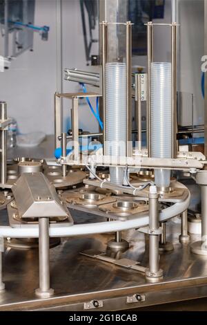 Fragment of a food industry production line for filling and packaging liquid products in plastic cups. Vertical image, close-up, copy space. Stock Photo