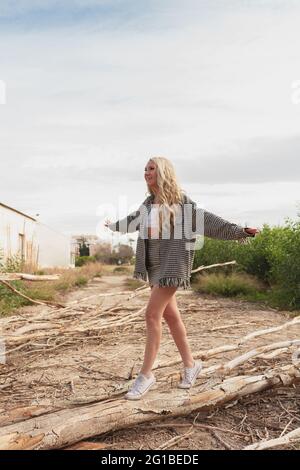 Full body of smiling female with outstretched arms balancing on log in rural area Stock Photo
