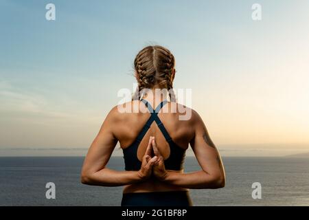 Back view of anonymous female with namaste hands practicing yoga against ocean in twilight in back lit Stock Photo