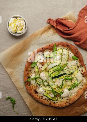 Top view of tasty pizza with squash slices and condiments with fresh arugula leaves on parchment paper on beige background Stock Photo