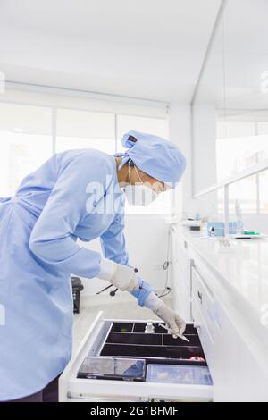 Side view of female orthodontist leaning forward above drawer with medical instruments at work in hospital Stock Photo