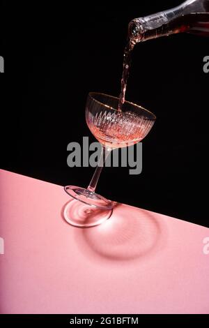 Anonymous person pouring rose sparkling wine into elegant coupe glass against two colored background Stock Photo