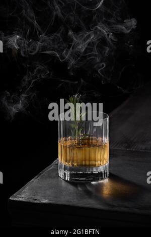 From above glass of cold whiskey decorated with green leaf placed on black table in dark smoky room Stock Photo