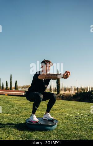 Determined male athlete with tattoos and outstretched arms training on spinner while looking forward in town Stock Photo