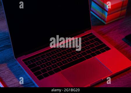 High angle of opened netbook with black screen placed on wooden table near note papers in dark workspace with neon lights Stock Photo