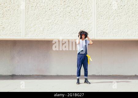 Smiling young ethnic male in retro wear touching curly hair while looking at camera on pavement Stock Photo