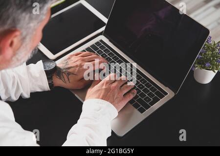From above cropped unrecognizable middle aged male entrepreneur in formal wear working on laptop at table in the office Stock Photo