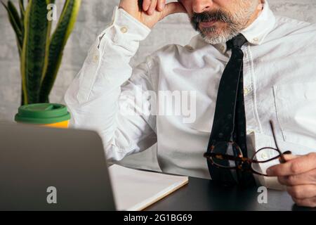Cropped unrecognizable thoughtful middle aged male entrepreneur in formal wear working on laptop at table in the office Stock Photo