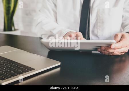 Crop anonymous male entrepreneur in white shirt surfing internet on tablet at desk with laptop during telework Stock Photo