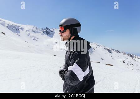 Side view of bearded male athlete in sports glasses and helmet admiring Sierra Nevada under cloudy blue sky in Spain Stock Photo