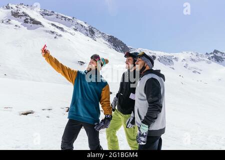 Content male friends in sports clothes taking self portrait on cellphone against Sierra Nevada in wintertime Stock Photo