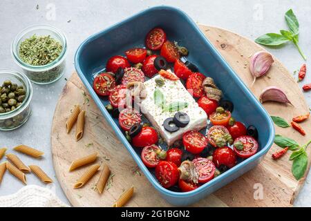 Top view of ripe cherry tomatoes with black olive slices and feta cheese in baking dish near uncooked penne Stock Photo