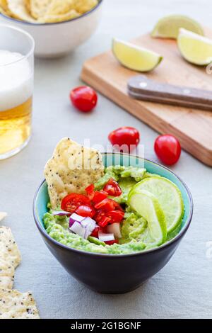 High angle of bowl with tasty guacamole with ripe cherry tomato and red onion near lime slices Stock Photo