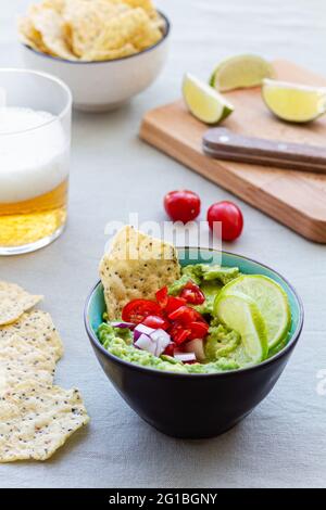 High angle of bowl with tasty guacamole with ripe cherry tomato and red onion near lime slices Stock Photo