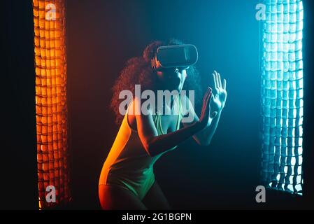 Anonymous astonished ethnic female with open mouth exploring virtual reality in headset on black background Stock Photo