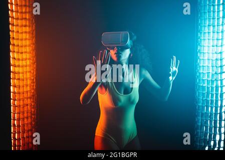Anonymous astonished ethnic female with open mouth exploring virtual reality in headset on black background Stock Photo