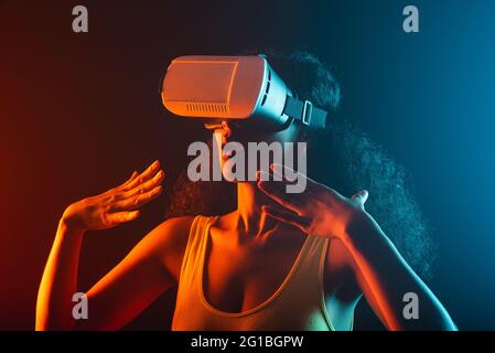 Anonymous astonished ethnic female with open mouth exploring virtual reality in headset on black background Stock Photo