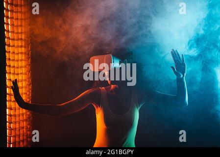 Anonymous astonished ethnic female with open mouth exploring virtual reality in headset on black background Stock Photo