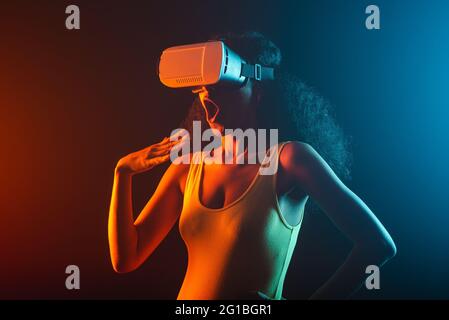 Anonymous astonished ethnic female with open mouth exploring virtual reality in headset on black background Stock Photo