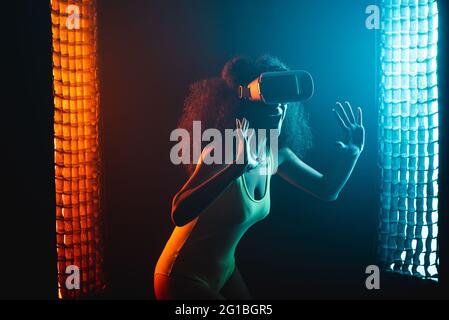 Anonymous astonished ethnic female with open mouth exploring virtual reality in headset on black background Stock Photo