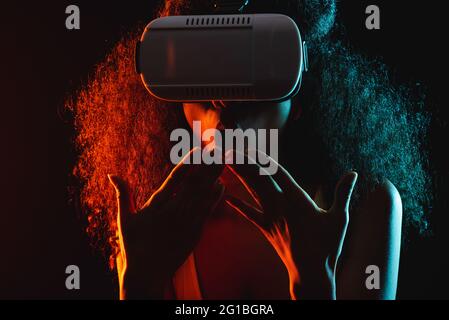 Anonymous astonished ethnic female with open mouth exploring virtual reality in headset on black background Stock Photo