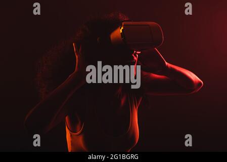 Anonymous astonished ethnic female with open mouth exploring virtual reality in headset on black background Stock Photo