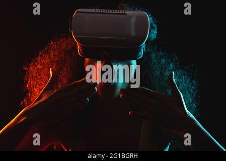 Anonymous astonished ethnic female with open mouth exploring virtual reality in headset on black background Stock Photo